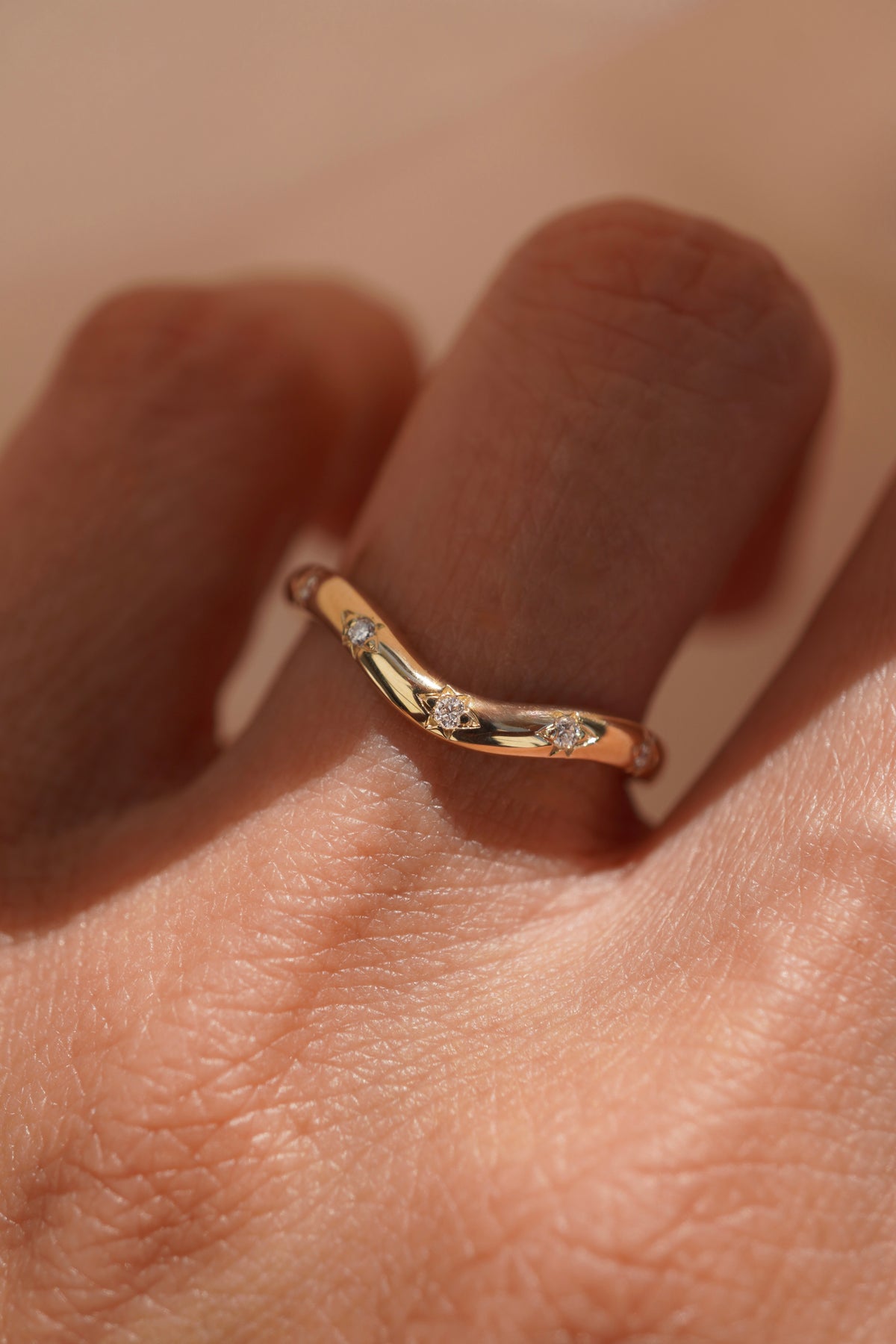 A close-up of a hand wearing a slim curved gold contour ring with round diamonds set within the band.